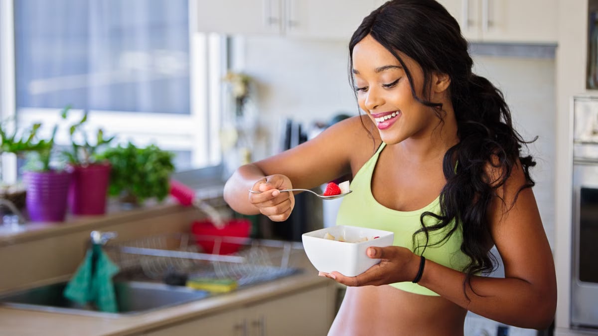 Cheerful woman enjoying fresh strawberries in a cozy kitchen setting. Promotes healthy living and happiness.