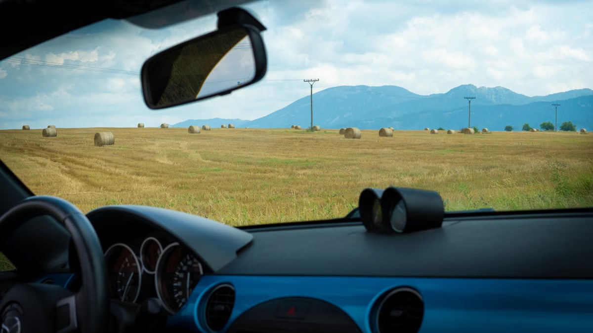 Interior view of a car on a rural road in Slovakia with hay bales and mountains in view.